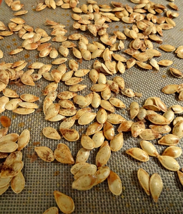 Raw, cleaned pumpkin seeds sprinkled with salt and chili powder on Silpat baking mat
